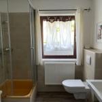 Bathroom with shower, toilet, and sink. Window with curtains and radiator.