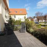 Terrasse mit Tisch und zwei Stühlen neben einem Haus mit Garten.