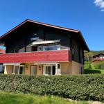 A two-story house with a red balcony and green hedge fence.