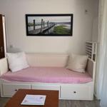 A bedroom with a white bed, pink bedding, and wall art of a pier.
