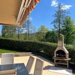 Terrace with table, chairs, and grill, view of greenery and water.