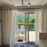 Living area with view of balcony and garden. Refrigerator, microwave, and sofa visible.