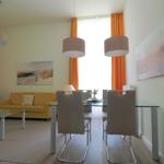 Wohn- und Essbereich mit Sofa, Tisch und Stühlen sowie Fenster mit orangefarbenen Vorhängen.