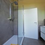 Duschkabine mit Glaswand, Waschbecken und Schrank in moderner Badezimmerausstattung.