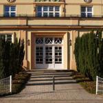 Haus mit Eingangstreppe, weißen Türen und hohen Zypressen