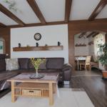 Living room with brown sofa, wooden beams, and table. Passage to dining area.
