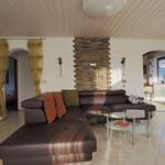 Living room with brown sofa, glass table, and stone wall. Doorways to bedroom and window area.