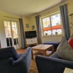 Wohnzimmer mit Sofa, Couchtisch und Fernseher. Durchgang zum Esszimmer und Terrasse.