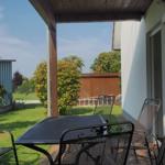 Terrasse mit Tisch und Stühlen, Blick auf grünen Garten und Zaun.