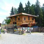Wooden house with balcony and sign in front of forest. Entrance area with fence and information boards.