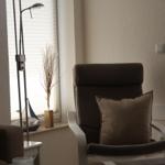 Ein Sessel mit Kissen steht vor einem Fenster mit Jalousie. Neben ihm steht eine Stehlampe.