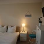 Schlafzimmer mit Bett, Nachttischen, Fernseher und Pflanze.