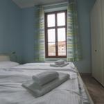 Schlafzimmer mit Bett, Gardinen und Kleiderschrank. Fensterblick auf Gebäude.