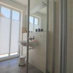 Badezimmer mit Dusche, Waschbecken und Toilette. Fenster mit Jalousie.