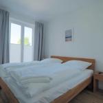 Schlafzimmer mit Holzbett, Fenster und Nachttisch.