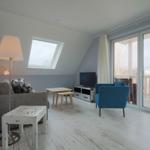 Wohnzimmer mit Sofa, blauem Sessel, TV und Balkonzugang.
