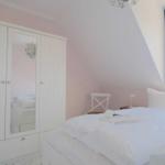 Schlafzimmer mit weißem Bett, Kleiderschrank und blauen Vorhängen an einem Fenster.
