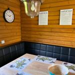Dining area with wooden walls, black cushioned benches, and table with olive motifs.