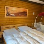 Bedroom with wooden walls, bed, nightstand, and crib.