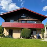 Two-story house with balcony, garden, and grill area under blue sky.