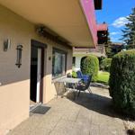 Entrance with terrace, table, chairs, and green hedge.