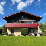 House with balcony, garden, and grill area under blue sky.