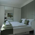 Schlafzimmer mit Bett, grünen Kissen und Spiegelschrank. Wandtapete mit Streifenmuster.