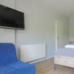 Zimmer mit Bett, Sofa und Wandfernseher. Holzboden und Kleiderschrank sichtbar.
