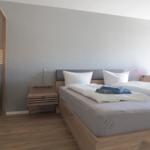 Schlafzimmer mit Bett, Nachttisch und Kleiderschrank. Holzboden und graue Wand.