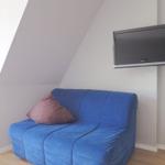 Ein blauer Sessel mit Kissen unter einer schrägen Decke. An der Wand hängt ein Fernseher.