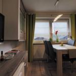 Dining area with table, chairs, and window. Green curtains and wooden floor.