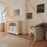 Wohnzimmer mit weißem Schrank, Sessel, Kleiderständer und Bildern an der Wand.