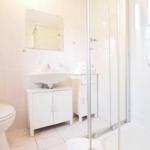 Badezimmer mit Dusche, Waschbecken und Toilette. Weiße Fliesen und Möbel.