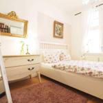 Schlafzimmer mit Bett, Schrank und Spiegel an der Wand. Fenster mit Vorhängen.
