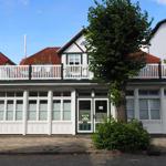 Haus mit weißem Balkon, rotem Dach und großen Fenstern an der Straße