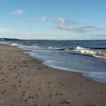 Strand mit Wellen und Spuren, ein Wanderer geht entlang des Wassers.