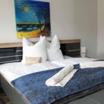 Doppelbett mit blauer Decke, weißen Kissen und Wandbild