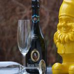 Auf einem Tisch steht eine Flasche Sekt, ein Glas und eine gelbe Gnome-Figur.