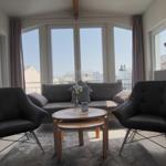 Ein Wohnzimmer mit Sofa, zwei Sesseln und einem runden Tisch. Große Fenster bieten Blick auf die Stadt.