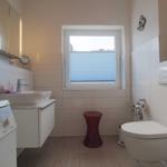 Badezimmer mit Waschbecken, Toilette und Fenster mit Jalousie.