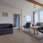 Wohnzimmer mit Sofa, Sessel und Tisch. Holzboden und große Fenster.