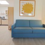 Blauer Sofa im Wohnbereich mit Küchenbereich im Hintergrund und Wandbild.
