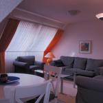 Wohnzimmer mit Sofa, Sessel, Esstisch und Fenster mit Vorhängen.