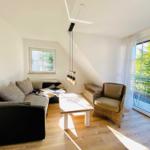 Wohnzimmer mit Sofa, Sessel und Balkon. Holzboden und Dachschrägen.