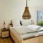 Schlafzimmer mit Doppelbett, Holzfußboden und Balkontür. Holzlampe hängt über dem Bett.