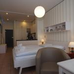 Schlafzimmer mit Bett, Schreibtisch und Küchenbereich im Hintergrund.