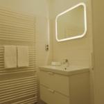 Badezimmer mit Waschtisch, Spiegel und Handtuchhalter.