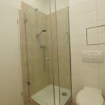 Dusche mit Glaswand, Toilette und Wandspiegel in Badezimmer.
