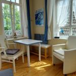 Ein Raum mit Tisch, Stühlen und Fernseher. Durch Fenster und Balkontür ist eine Terrasse sichtbar.