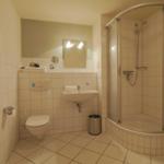 Badezimmer mit Dusche, Waschbecken und Toilette. Fliesenwand und Boden.